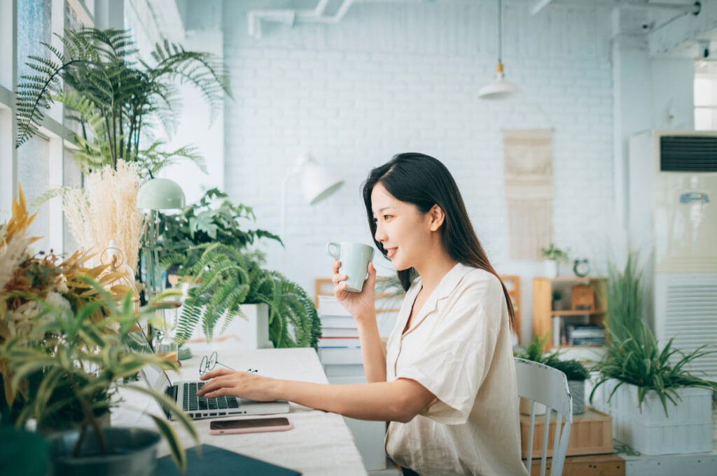 A woman is sitting in front of a desk and a laptop with lots of plants in her office space.